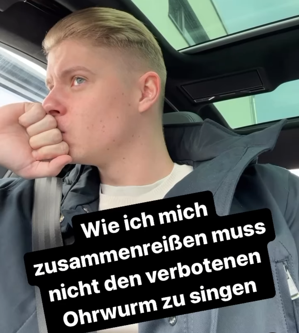 Bild von KuchenTV: Er sitzt im Auto und hält seine Faust vor seinen Mund darunter der Text " Wie ich mich zusammenreisen muss nicht den verbotenen Ohrwurm zu singen".